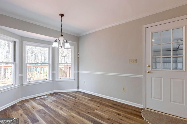 unfurnished dining area with visible vents, baseboards, wood finished floors, an inviting chandelier, and crown molding