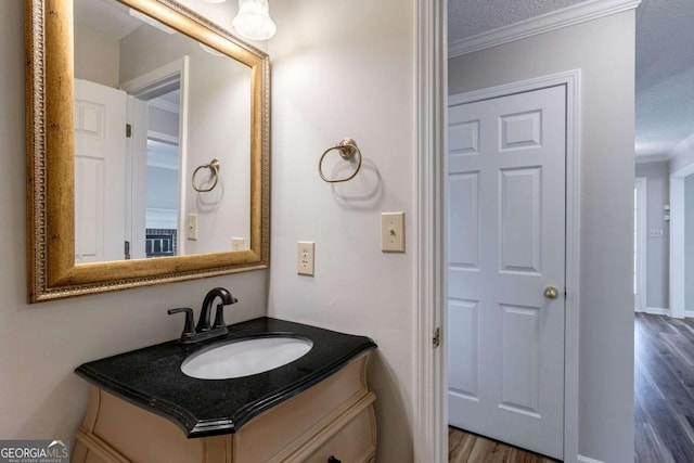 bathroom with a textured ceiling, ornamental molding, wood finished floors, and vanity