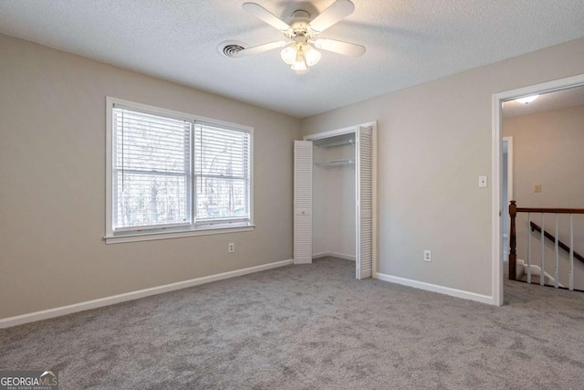 unfurnished bedroom featuring a textured ceiling, light carpet, visible vents, baseboards, and a closet