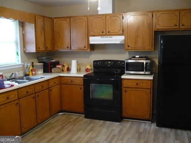 kitchen with light wood-style flooring, under cabinet range hood, a sink, light countertops, and black appliances