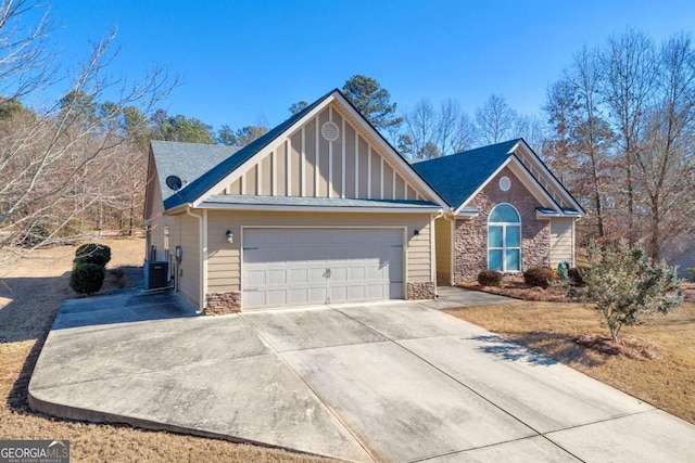 view of front of house with board and batten siding, central AC, a garage, stone siding, and driveway