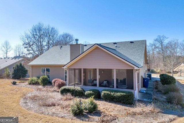 back of house featuring a shingled roof, a chimney, and a sunroom