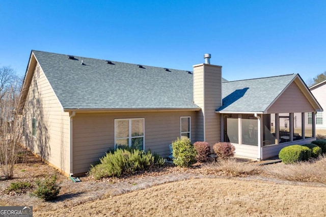 back of property featuring a sunroom, roof with shingles, and a chimney