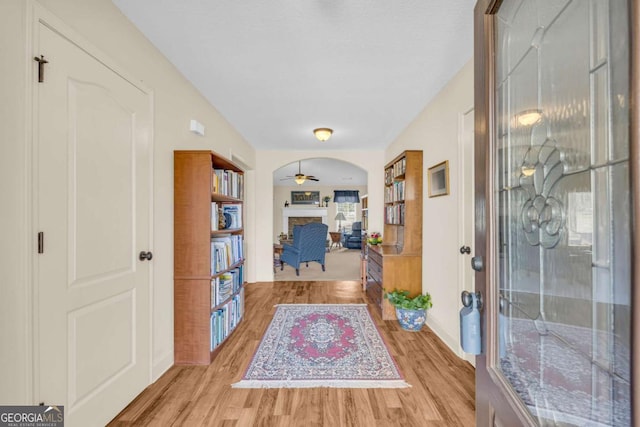 entrance foyer featuring arched walkways, a stone fireplace, light wood finished floors, and ceiling fan