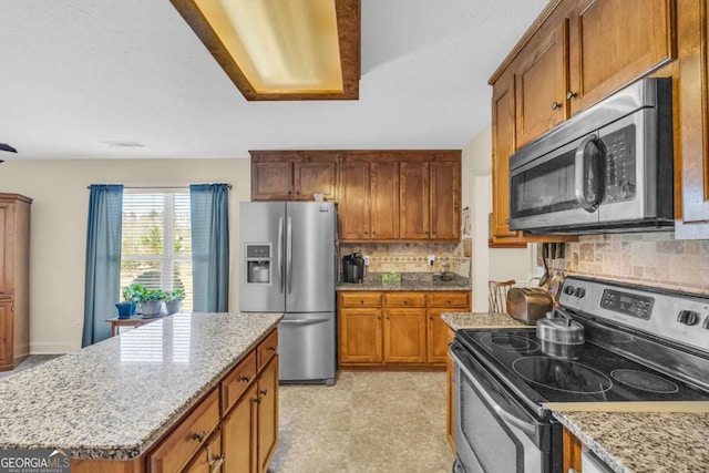 kitchen featuring appliances with stainless steel finishes, brown cabinetry, a kitchen island, and light stone counters