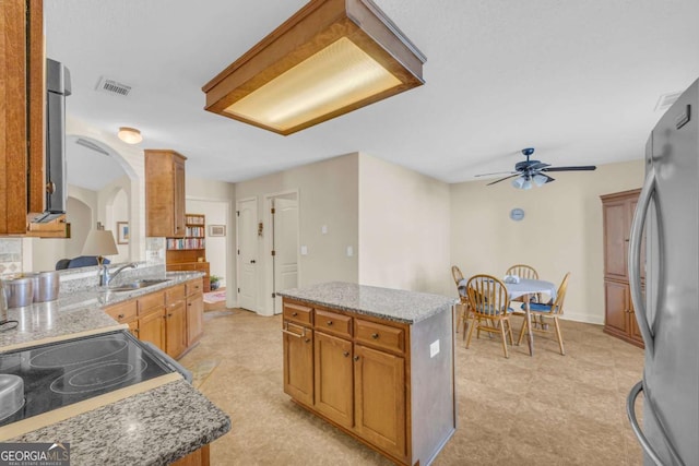 kitchen with a kitchen island, freestanding refrigerator, and light stone countertops