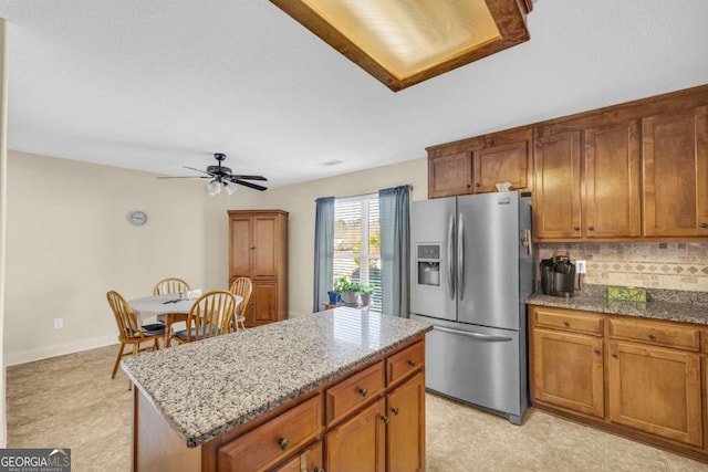 kitchen featuring brown cabinets, a center island, stainless steel fridge, and light stone countertops