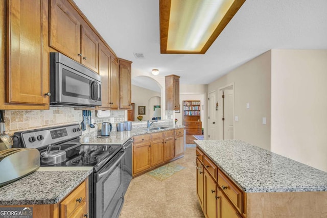 kitchen featuring stainless steel appliances, brown cabinets, a sink, and decorative columns