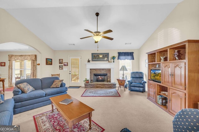 living area with light carpet, a fireplace, plenty of natural light, and arched walkways