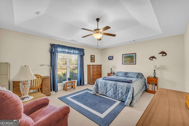 bedroom with light carpet, visible vents, a tray ceiling, and a ceiling fan