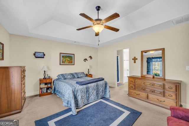 bedroom with a tray ceiling, light colored carpet, visible vents, ceiling fan, and baseboards