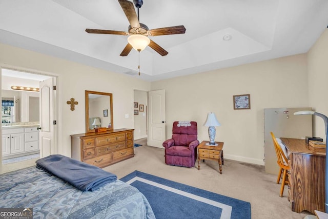 bedroom with light carpet, baseboards, a raised ceiling, a ceiling fan, and ensuite bath