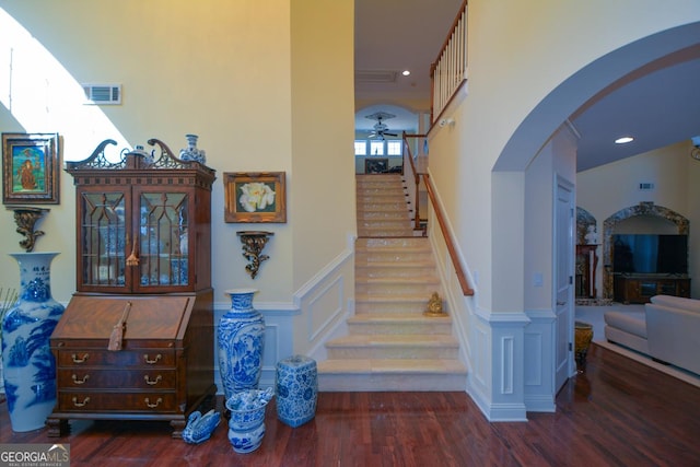 stairs featuring arched walkways, a wainscoted wall, visible vents, a decorative wall, and wood finished floors