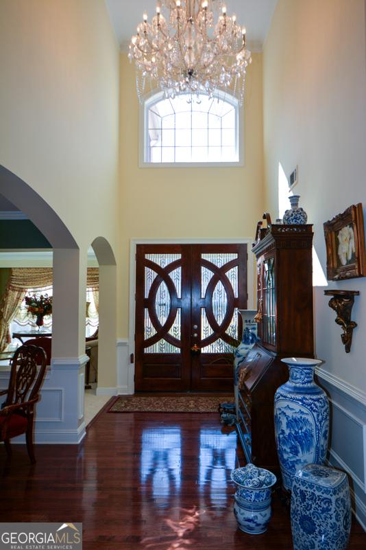 foyer entrance featuring a towering ceiling, dark wood-style floors, arched walkways, and wainscoting