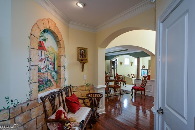 hall with arched walkways, wainscoting, ornamental molding, wood finished floors, and a decorative wall