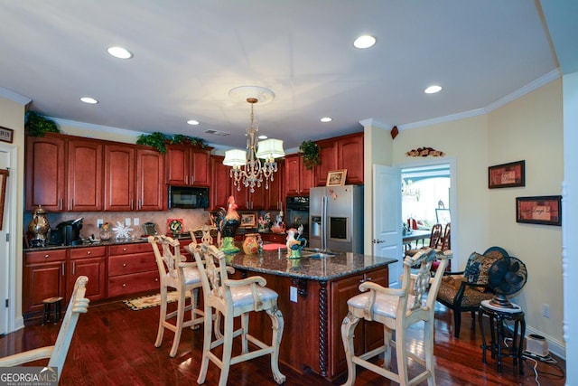 kitchen featuring stainless steel fridge, an island with sink, ornamental molding, hanging light fixtures, and black microwave