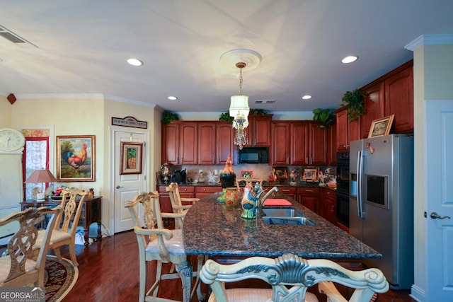 kitchen featuring dark wood-type flooring, decorative light fixtures, a kitchen island with sink, black appliances, and a sink