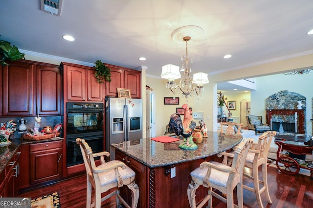 kitchen featuring decorative light fixtures, visible vents, dobule oven black, dark stone countertops, and stainless steel fridge with ice dispenser