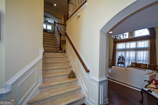 stairs with arched walkways, a decorative wall, wood finished floors, visible vents, and wainscoting