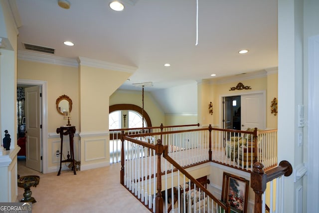 hall featuring a decorative wall, light carpet, an upstairs landing, visible vents, and crown molding