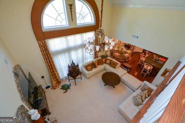 carpeted living room with a high ceiling, visible vents, a notable chandelier, and ornamental molding