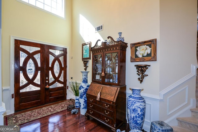 entryway featuring wainscoting, stairway, wood finished floors, a high ceiling, and a decorative wall