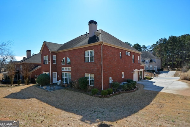 view of side of home with driveway, an attached garage, a chimney, and brick siding