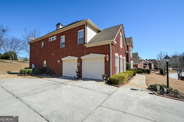 view of side of property with concrete driveway, brick siding, a chimney, and an attached garage