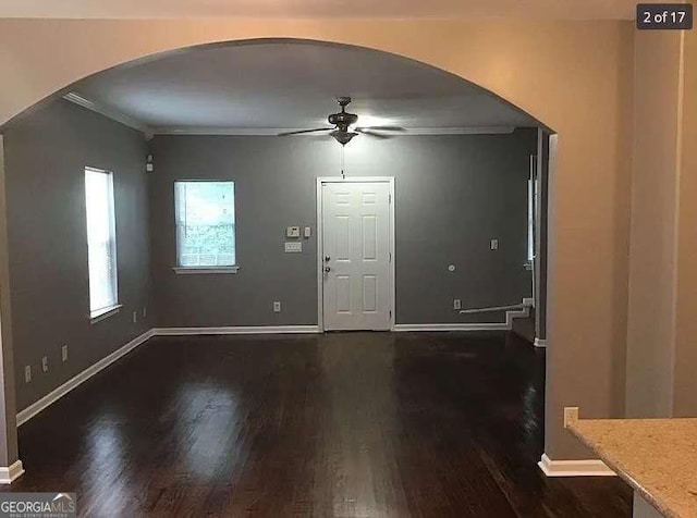 entryway featuring arched walkways, dark wood-type flooring, a ceiling fan, baseboards, and crown molding