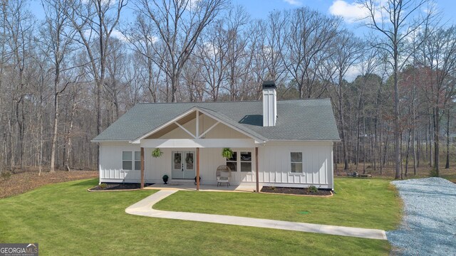 back of property with roof with shingles, a chimney, board and batten siding, and french doors