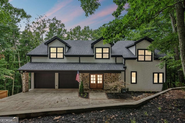 view of front of house with stone siding, roof with shingles, driveway, and french doors