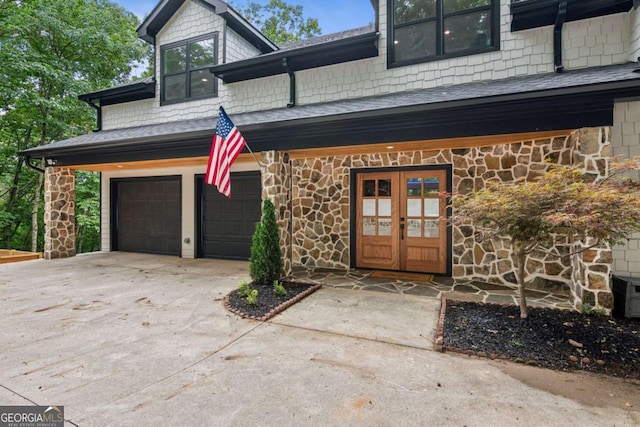 property entrance featuring french doors, roof with shingles, a garage, stone siding, and driveway