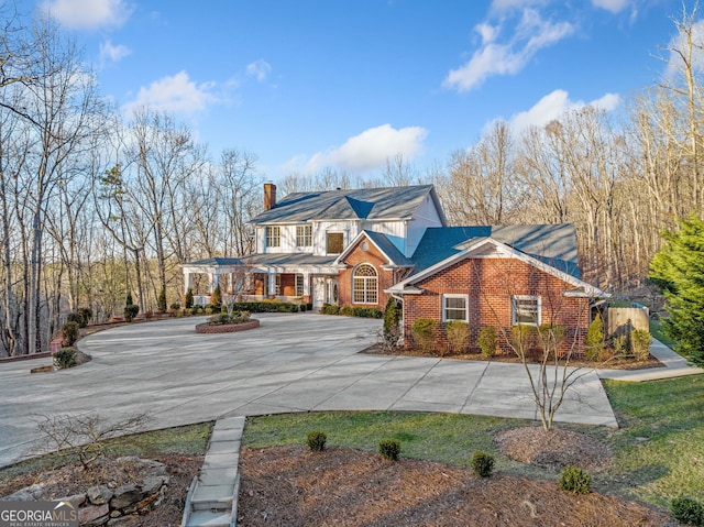 view of front of house featuring a chimney, concrete driveway, and brick siding