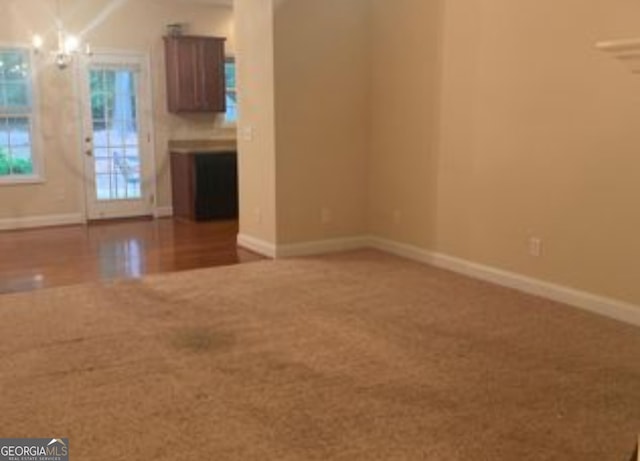 unfurnished living room with a chandelier, carpet flooring, and baseboards