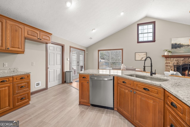 kitchen featuring brown cabinetry, a sink, a stone fireplace, light stone countertops, and dishwasher