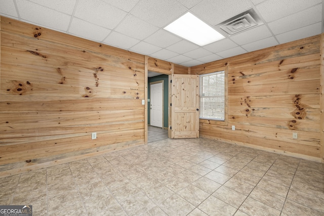 spare room with a paneled ceiling, wooden walls, visible vents, and tile patterned floors