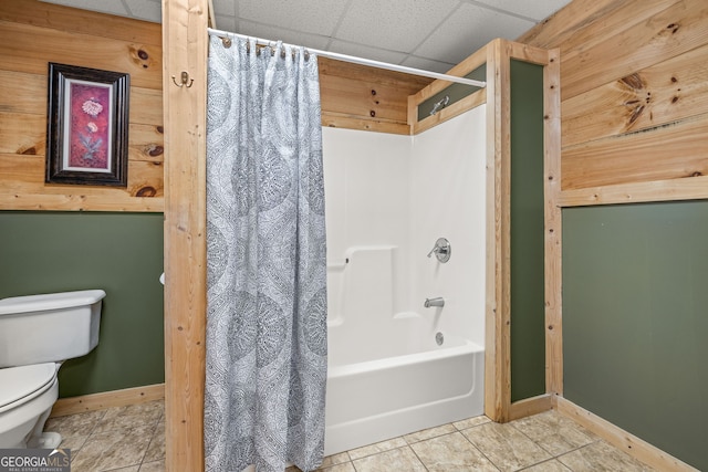 full bathroom featuring a drop ceiling, tile patterned flooring, toilet, baseboards, and shower / bath combo with shower curtain