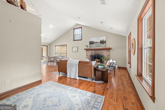living area featuring lofted ceiling, a warm lit fireplace, visible vents, and wood finished floors