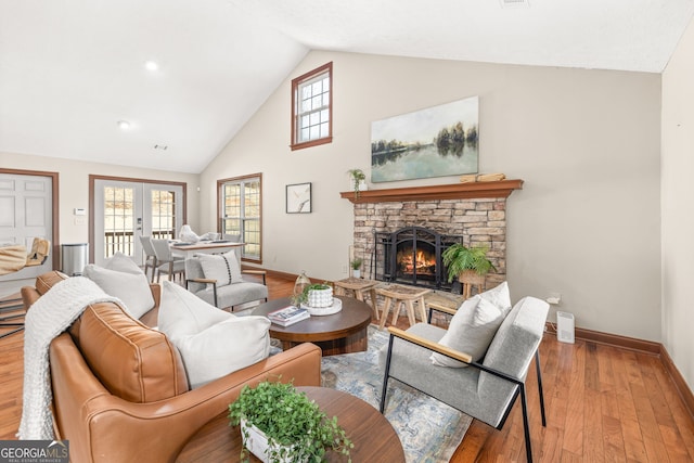 living area with baseboards, french doors, a stone fireplace, light wood-type flooring, and high vaulted ceiling