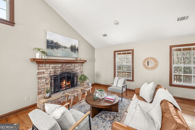 living area with a warm lit fireplace, wood finished floors, and visible vents