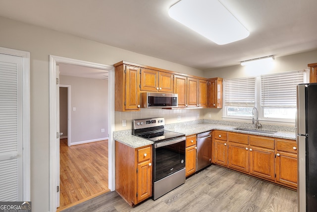 kitchen featuring appliances with stainless steel finishes, brown cabinetry, a sink, and light wood finished floors