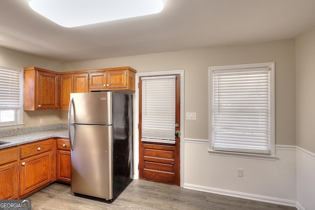 kitchen featuring light wood finished floors, baseboards, brown cabinetry, and freestanding refrigerator