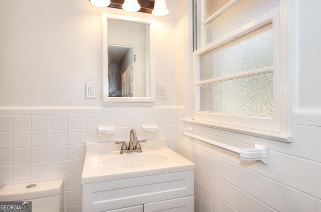 bathroom featuring toilet, wainscoting, tile walls, and vanity