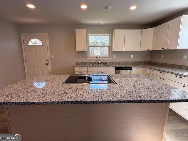 kitchen with light stone counters, white cabinets, a kitchen island, and a sink