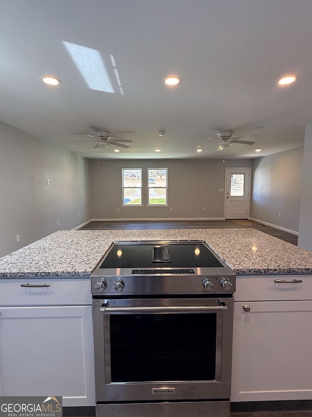 kitchen with open floor plan, high end stainless steel range oven, light stone countertops, and white cabinets