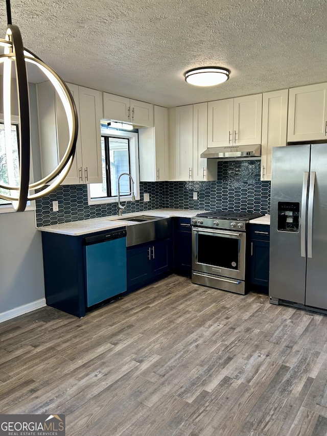 kitchen with stainless steel appliances, light countertops, white cabinetry, a sink, and under cabinet range hood