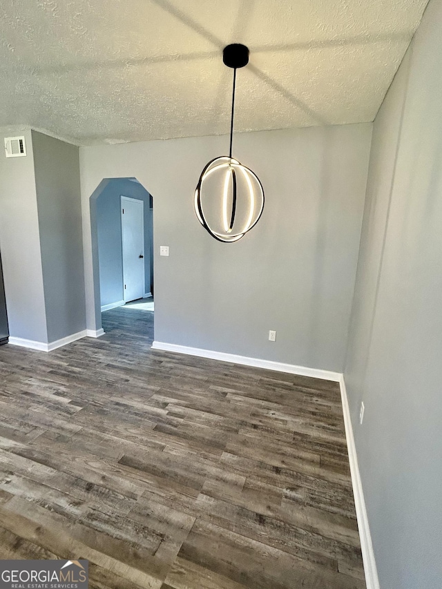 unfurnished dining area with baseboards, visible vents, arched walkways, and dark wood-type flooring