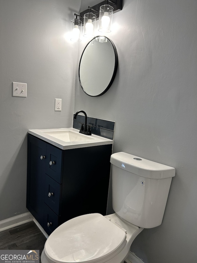 half bathroom featuring baseboards, vanity, toilet, and wood finished floors