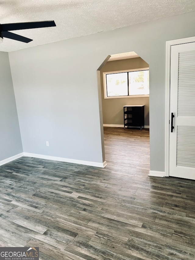 spare room with dark wood-style floors, baseboards, and arched walkways