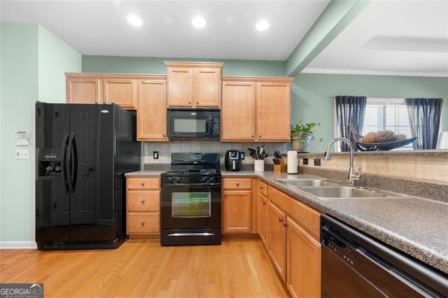 kitchen featuring black appliances, a sink, light wood-style flooring, and decorative backsplash